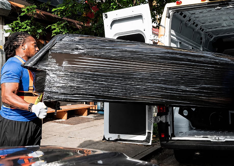 A professional mover loading a large and heavy-wrapped furniture into a delivery van. — Lugg