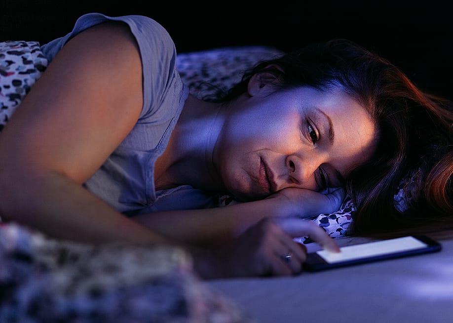 A stressed woman struggling to keep up with phone at night. — Marjan Apostolovic // Shutterstock