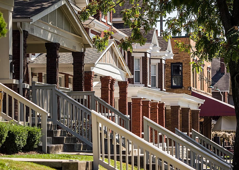 A row of American homes featuring front porches with brick columns and wooden railings. — Mario Cuitino // Shutterstock