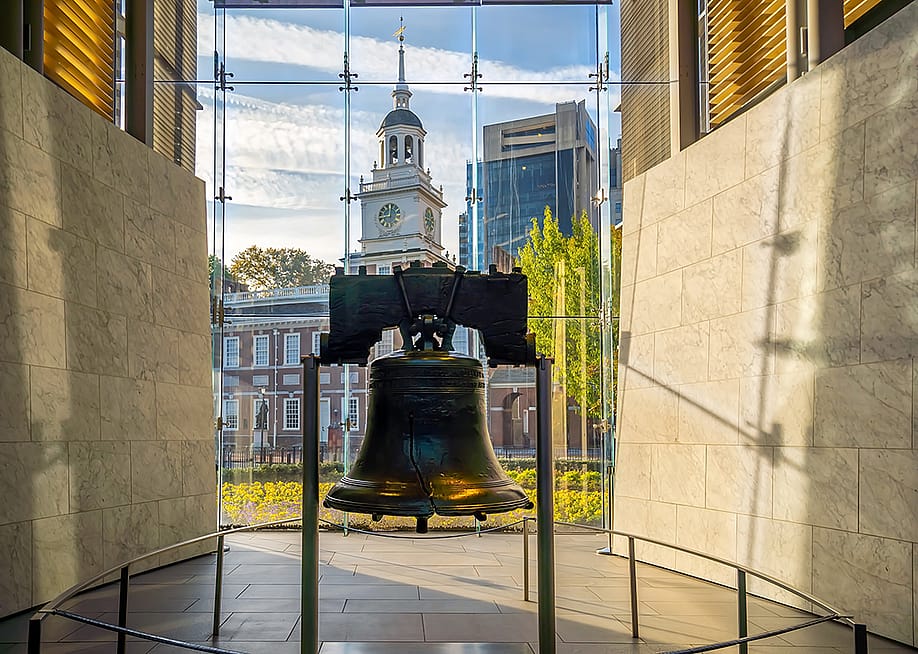 The Liberty Bell displayed inside the glass pavilion of the Liberty Bell Center, with the Independence Hall at the back in Philadelphia, Pennsylvania, USA. — f11photo // Shutterstock