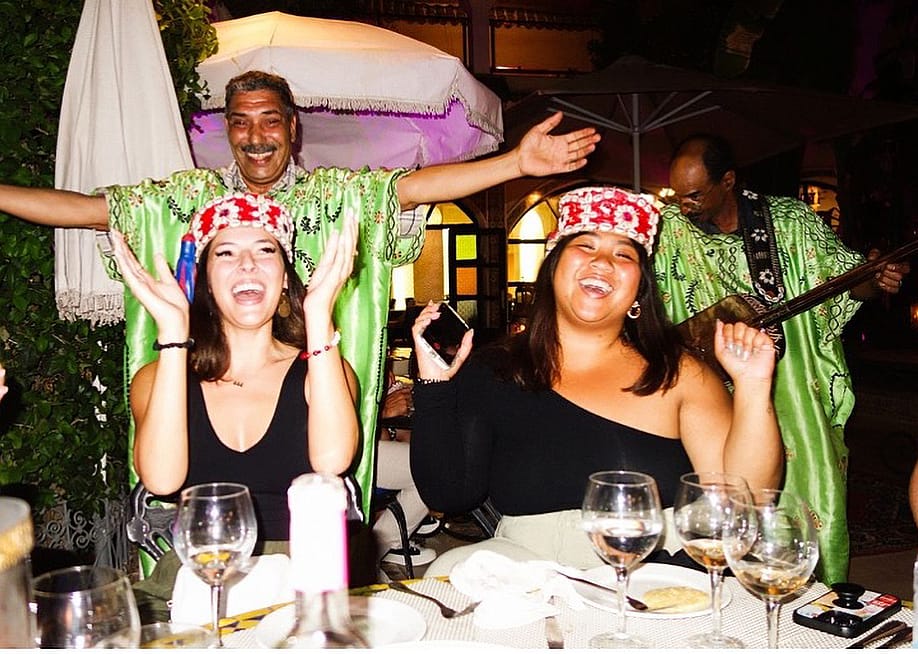 Two friends enjoying a festive performance by traditional musicians at the back during an outdoor dinner. — Courtesy of EF Ultimate Break