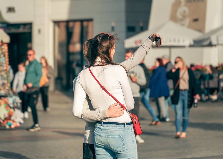 A Gen Z couple taking a smartphone selfie in a famous city spot during their vacation. — Alex Boc // Shutterstock