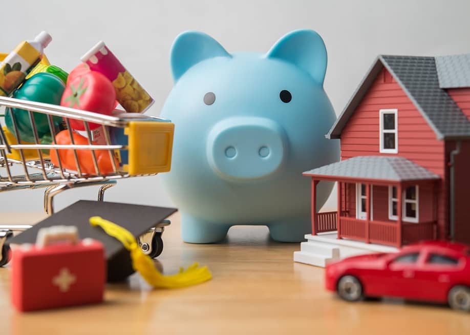 Physical figures of expense concepts such as mortgage, car, groceries around a piggy bank as a concept of budgeting and saving. — Pla2na // Shutterstock