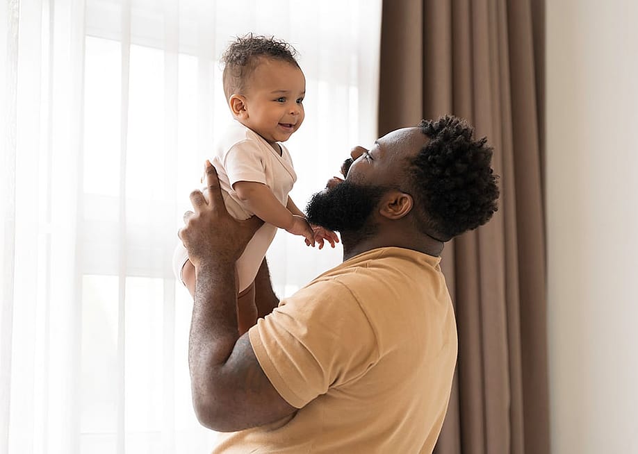 A father happily carrying his baby in the bedroom. — Amorn Suriyan // Shutterstock