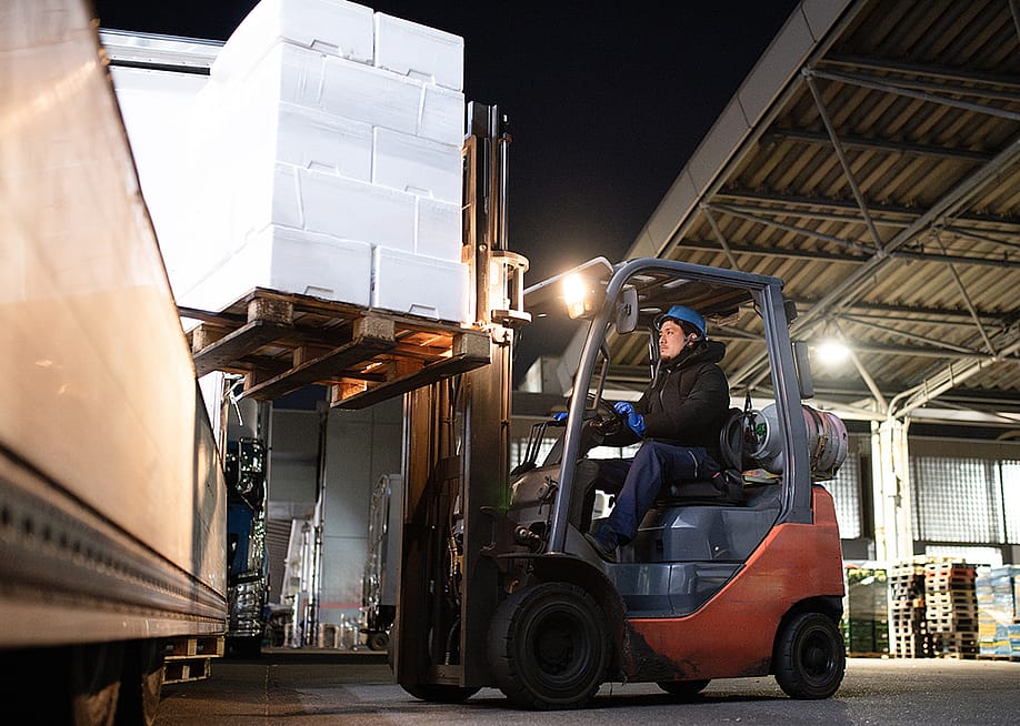 A warehouse officer operating a forklift and loading cargos to a truck. — Hakase_420 // Shutterstock
