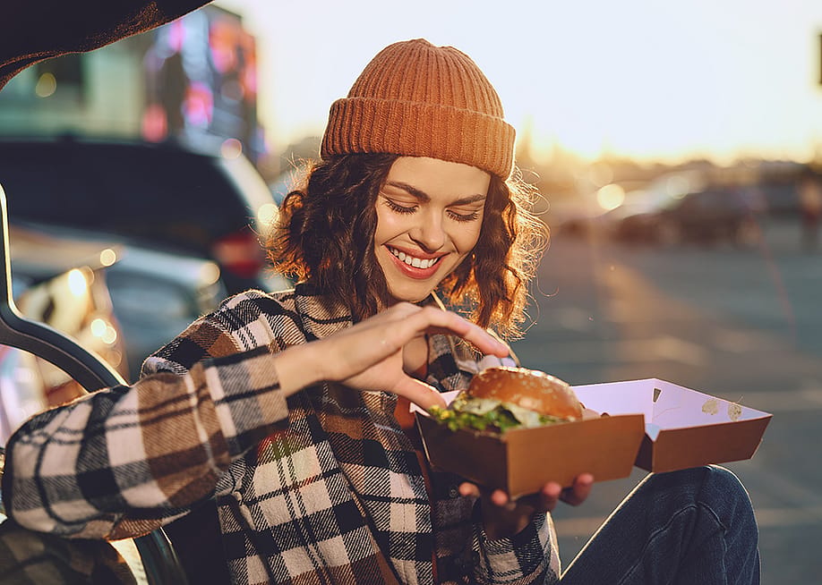 A young woman happily eating a takeout burger. — ShotPrime Studio // Shutterstock