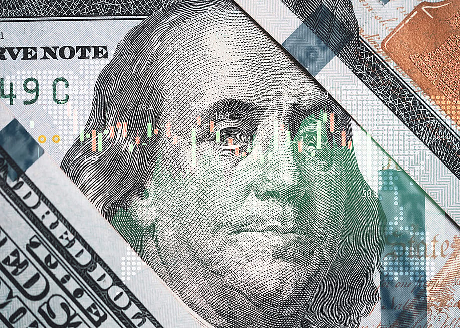 A close-up of Benjamin Franklin's face on a U.S. 100-dollar bill overlaid with a stock market trading chart. — Dilok Klaisataporn // Shutterstock