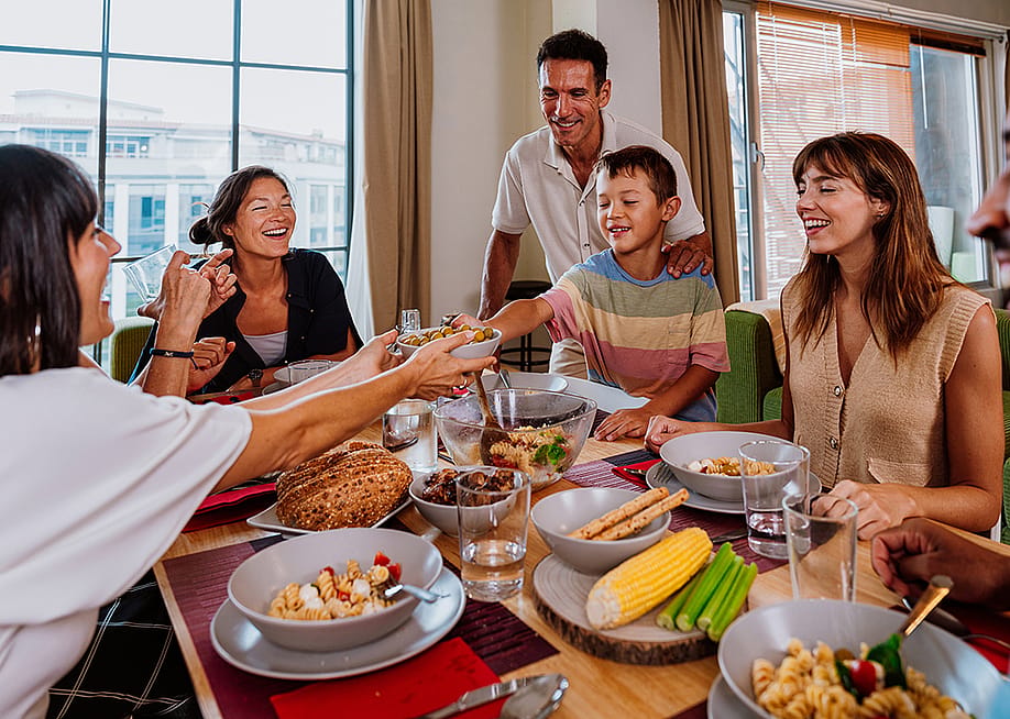 A diverse, multigenerational family sharing meals at the dinner table. — oneinchpunch // Shutterstock