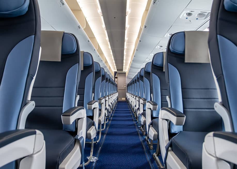 An interior cabin of an empty commercial aircraft lining a central aisle. — Dushlik // Shutterstock