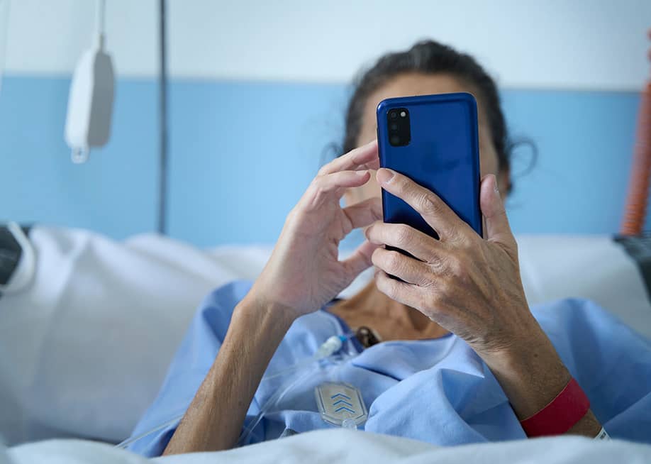 An elderly woman in a hospital bed checking her smartphone. — Carlos_Pascual // Shutterstock