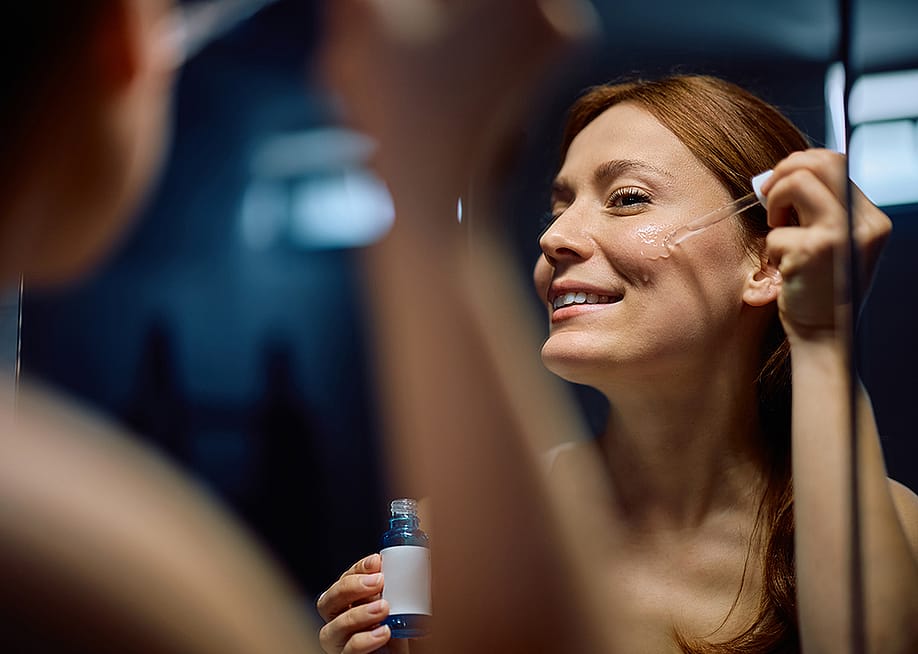 A person applying a moisturizing facial serum with a dropper in front of a mirror. — Drazen Zigic // Shutterstock