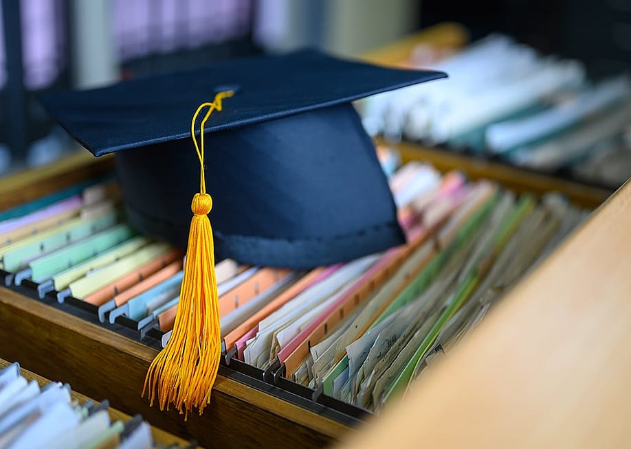 A black graduation cap placed on top of piles of documents. — Nirat.pix // Shutterstock