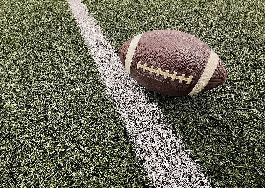 An American football seen on an artificial grass next to a white yard line. — Andrew Angelov // Shutterstock