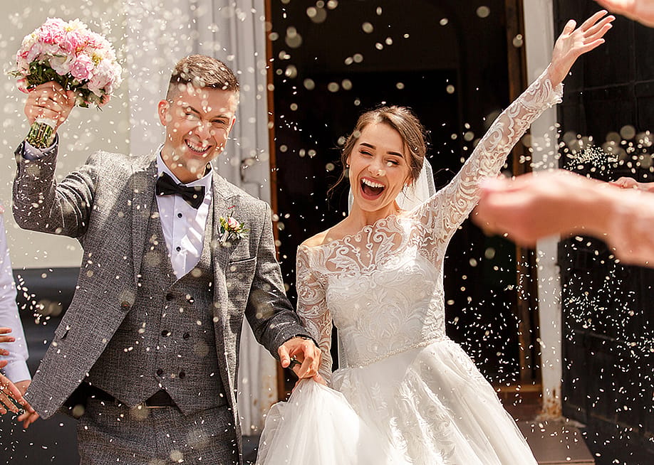 A newlywed couple celebrating after the ceremony while guests shower them with confetti. — Wedding and lifestyle // Shutterstock
