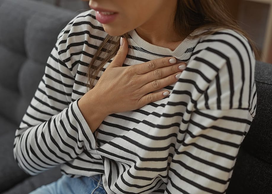 A person experiencing a heartburn with her hand pressed on the chest at home. — Krakenimages.com // Shutterstock