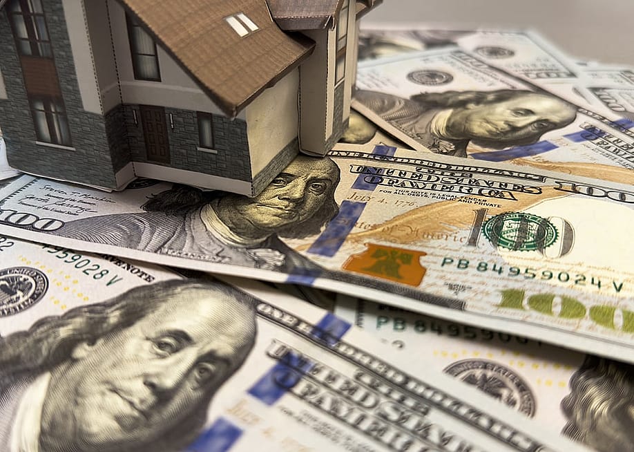 A miniature house above U.S. dollar bills, representing home equity and housing on credit concepts. — Andrew Angelov // Shutterstock