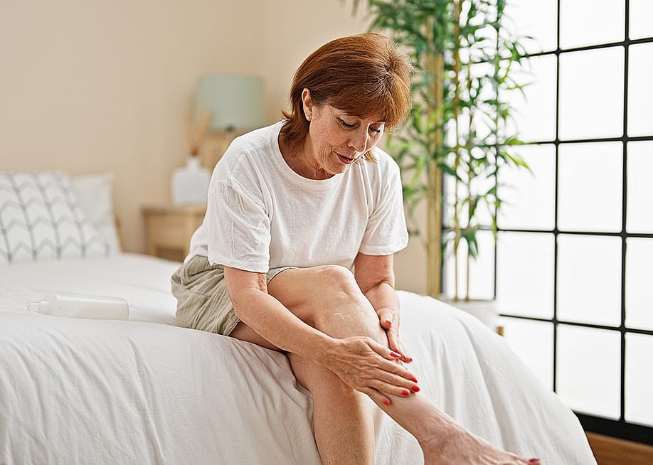 A middle-aged woman applying lotion on her legs at home. — Krakenimages.com // Shutterstock