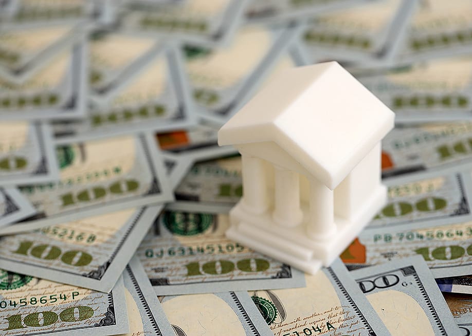 A miniature bank placed on US dollar bills, representing banking loan for business concepts. — Mehaniq // Shutterstock