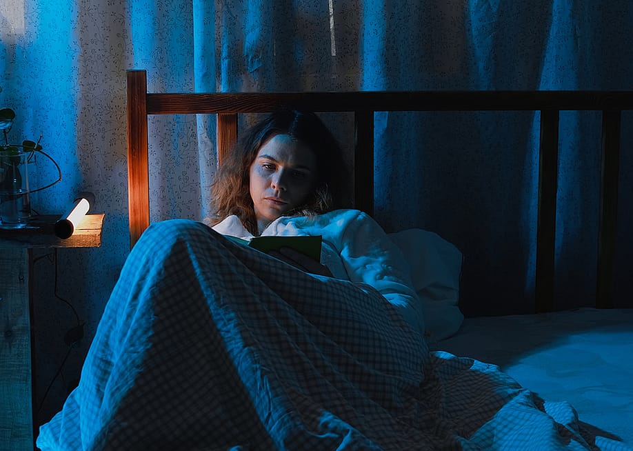A young adult suffering from insomnia while reading a book in bed at night. — Meteoritka // Shutterstock