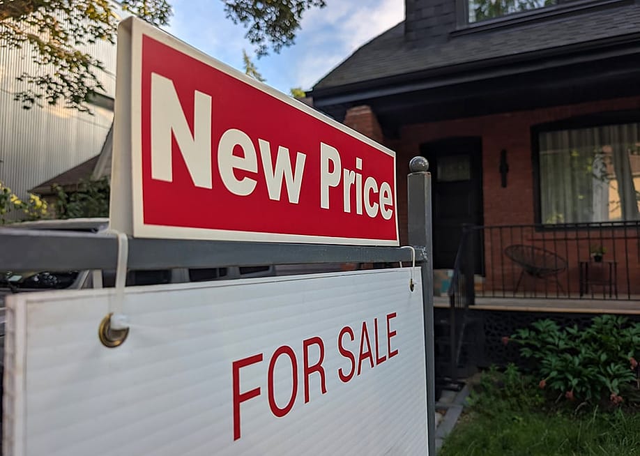 A sign for a new price sale displayed in a front yard of a single-detached residential house. — Elena Berd // Shutterstock