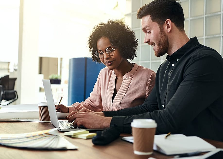 Two employees collaborating over financial data accounting and reviews from a laptop in an office. — Ground Picture // Shutterstock