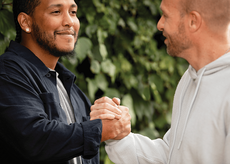 Two men greeting each other with a handshake outdoors — The Ad Council