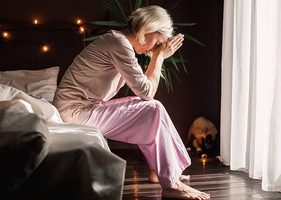 A stressed middle-aged woman sitting on her bed at home. — Gladskikh Tatiana // Shutterstock.