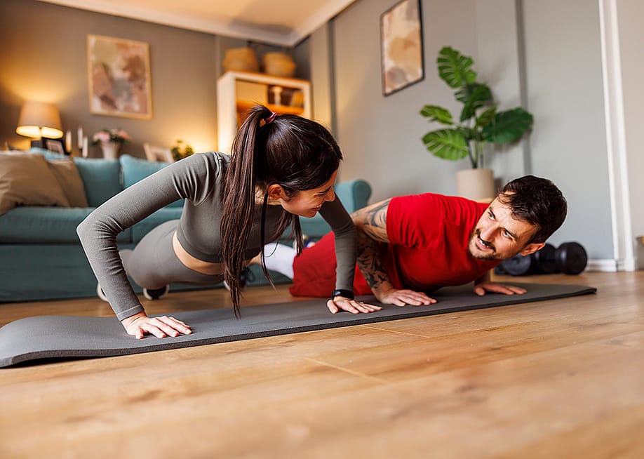 A young couple doing a push-up exercise together during their home workout session. — Impact Photography // Shutterstock