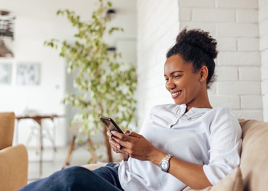 A person lounging comfortably in a sofa while browsing through her smartphone. — Branislav Nenin // Shutterstock