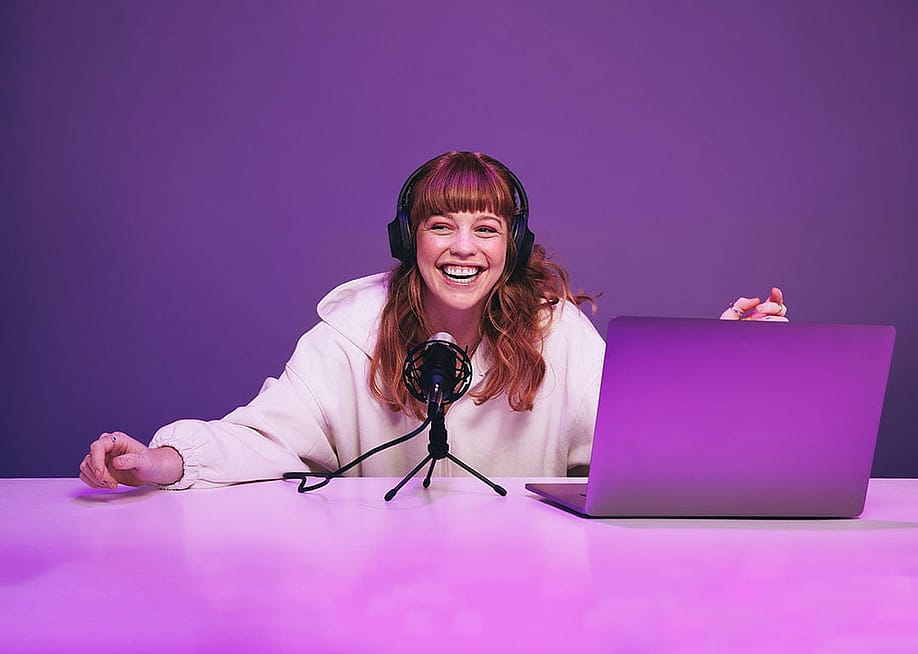 A happy young woman laughing while recording a live radio show in a studio. — Jacob Lund // Shutterstock