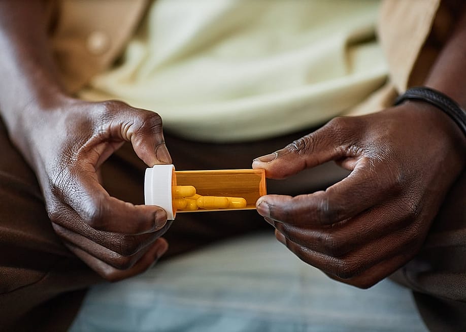 A patient holding a plastic medicine bottle with prescription pills in a clinic. — SeventyFour // Shutterstock