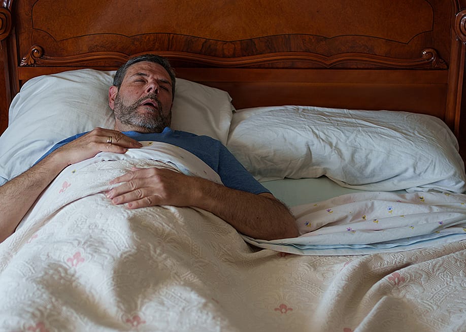 An elderly person sleeping on a bed and lying flat on their back. — Alejandro M. Ferrer // Shutterstock