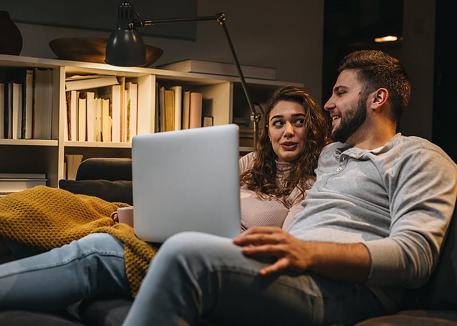 A young couple engaged in a discussion at home while relaxing in a sofa and viewing a laptop together. — Dejan Dundjerski // Shutterstock