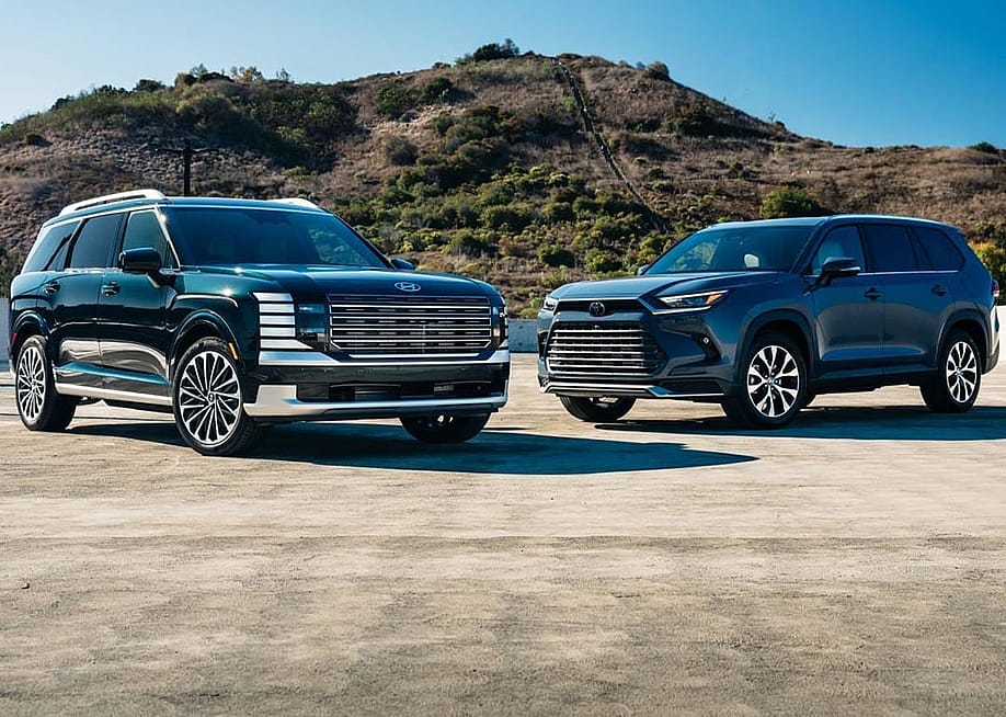 A 2026 Hyundai Palisade Calligraphy Hybrid and a 2025 Toyota Grand Highlander Hybrid parked in a concrete lot. — Courtesy of Edmunds