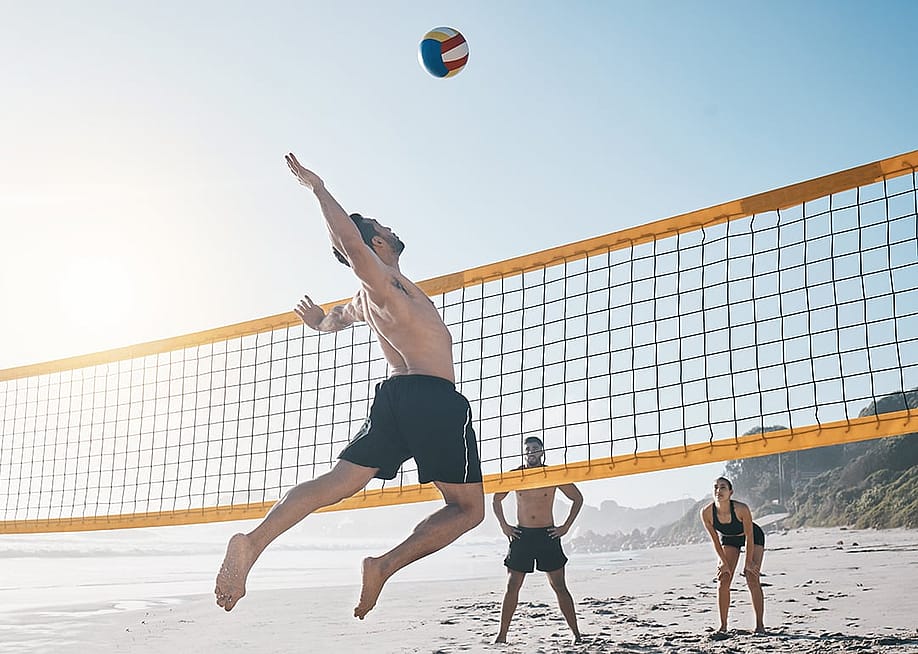 A person jumping for the ball during a beach volleyball match with friends. — PeopleImages // Shutterstock