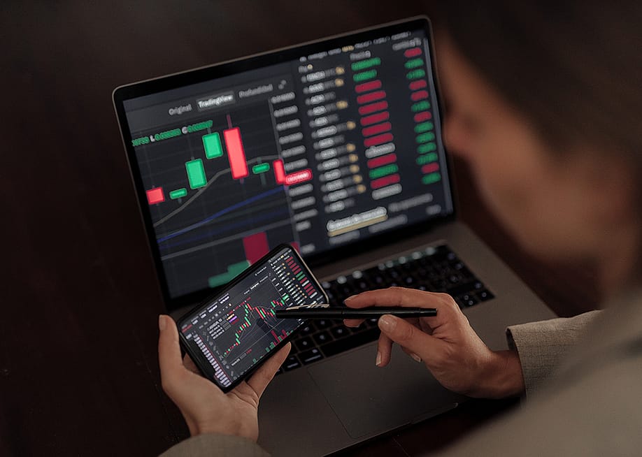 Person analyzing stock market charts on phone and laptop. — Cavan-Images // Shutterstock