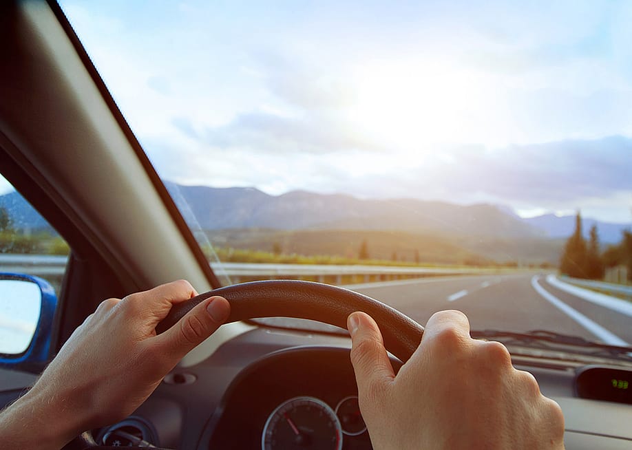 A driver's hands seen on the steering wheel of a car and an empty road ahead. — Song_about_summer // Shutterstock