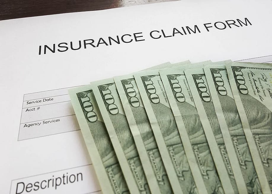 An insurance claim form and U.S. dollar bills placed above the blank document. — zimmytws // Shutterstock