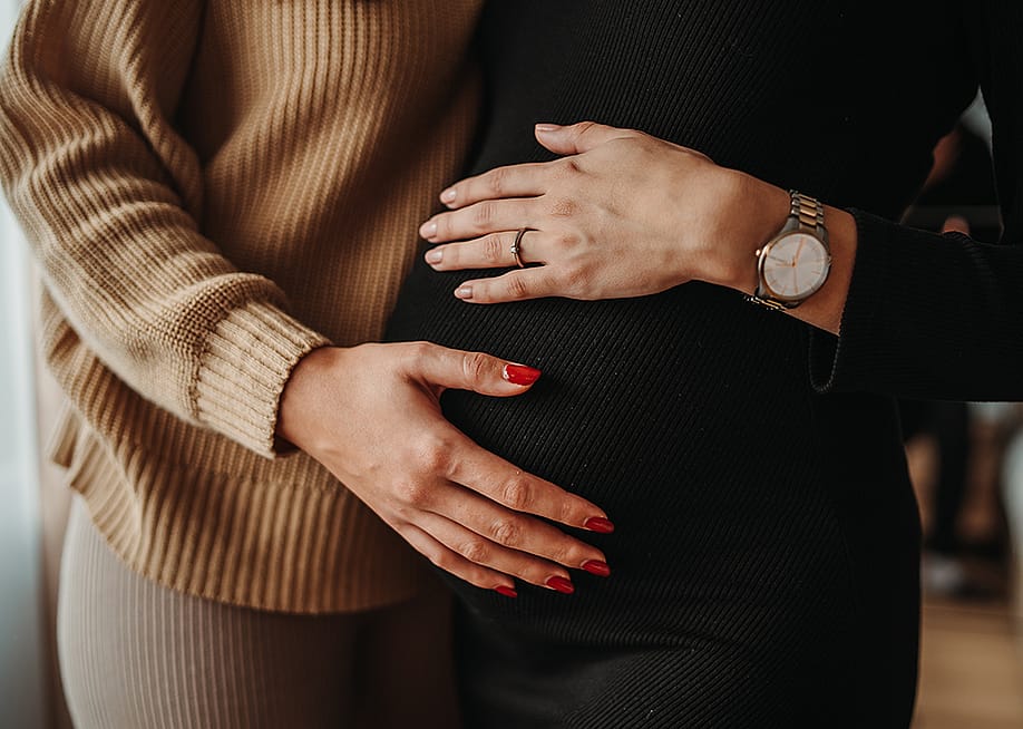 A genetic mother gently cradling the growing baby bump of her surrogate. — DukiPh // Shutterstock