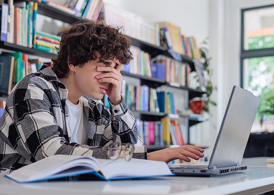 A tired student rubbing his eyes while studying on his laptop in the library. — Mishchenko Svitlana // Shutters