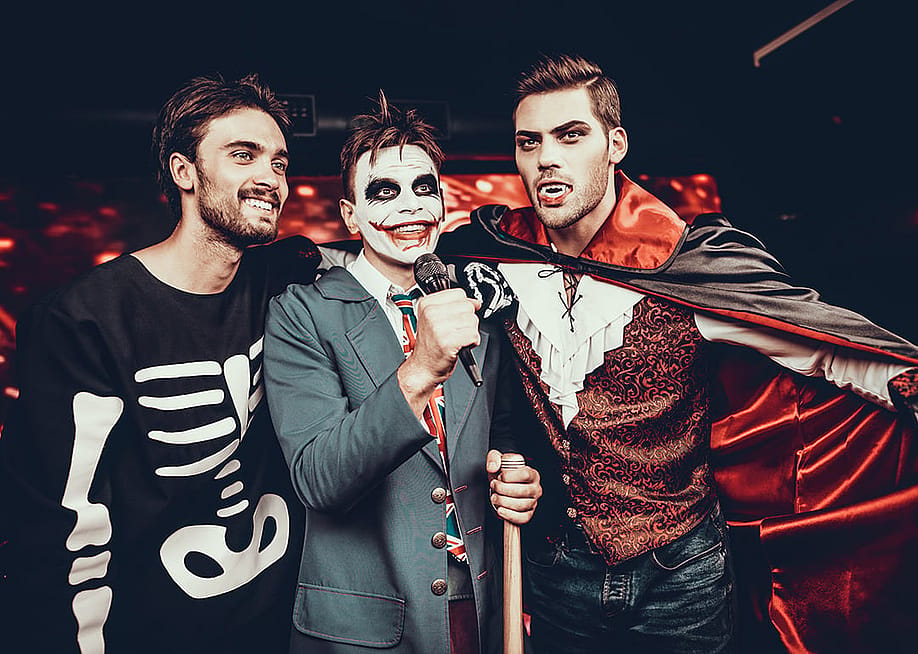 Young adults wearing Halloween costumes and singing karaoke at a party in a nightclub. — Vadym Huzhva // Shutterstock