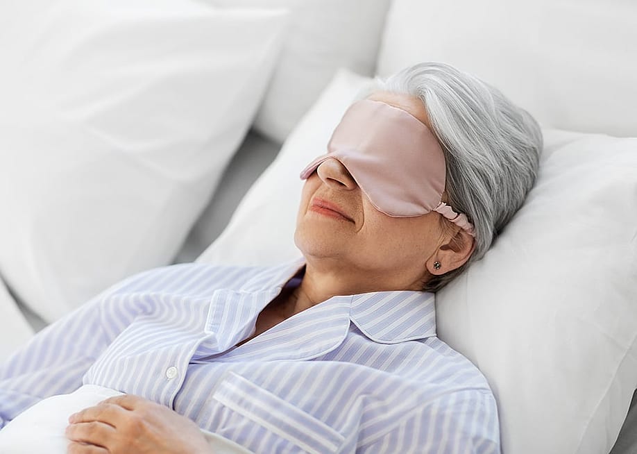 An elderly person sleeping with an eye mask in the home bedroom. — Ground Picture // Shutterstock