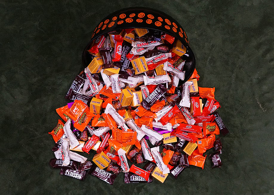 A variety of chocolates and candies spilling from a Halloween basket onto a flat surface. — Khairil Azhar Junos // Shutterstock