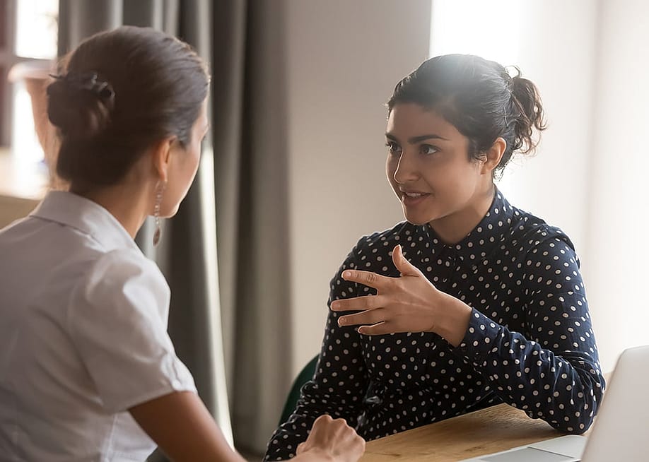 Coworkers sharing personal moments at work privately in a meeting room. — fizkes // Shutterstock