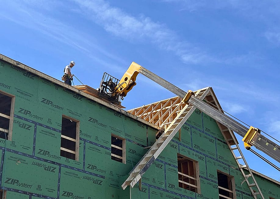 A construction worker retrieves plywood sheets lifted to the roof of a an affordable housing complex for seniors under construction in Portsmouth, Rhode Island, one of four states that have housing measures on the ballot this November. — Janine L. Weisman // Rhode Island Current