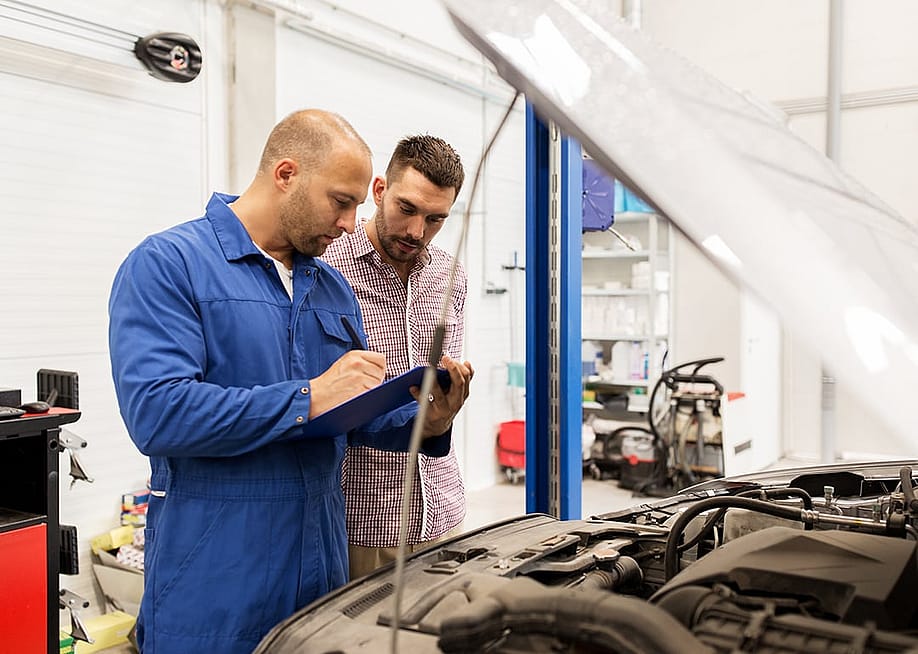 A mechanic taking notes to a clipboard while discussing repairs and management to the owner in the car shop. — Ground Picture // Shutterstock