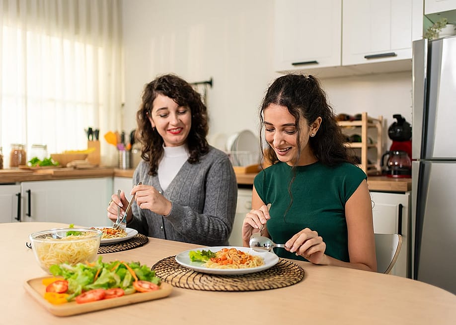 A parent and her young adult child enjoying homemade meals together in the dining table. — Hananeko_Studio // Shutterstock