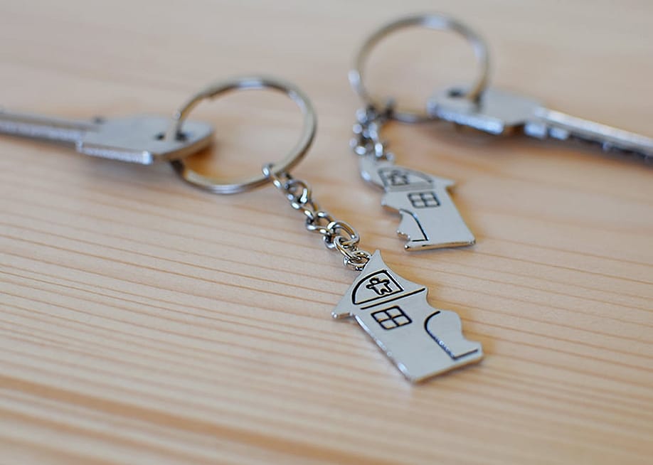 Two keys with divided house pendants on a wooden floor, representing a concept of division of shared property. — ingae // Shutterstock