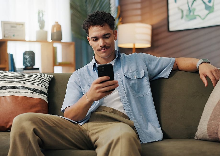 A person using social media from his smartphone while lounging in a sofa at home. — PeopleImages // Shutterstock