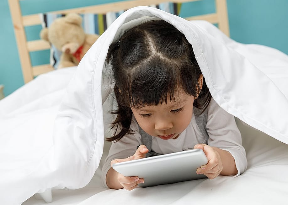 A toddler using a digital tablet under a blanket in a bed. — DONOT6_STUDIO // Shutterstock